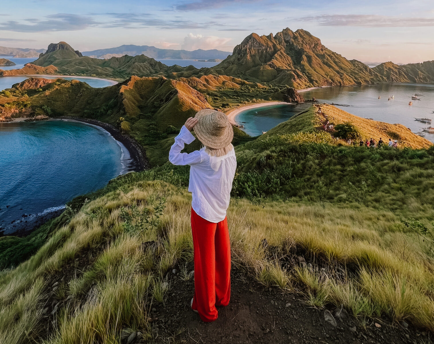 Sofia in a straw hat and red trousers overlooking the bays of Padar Island, Komodo National Park, Indonesia